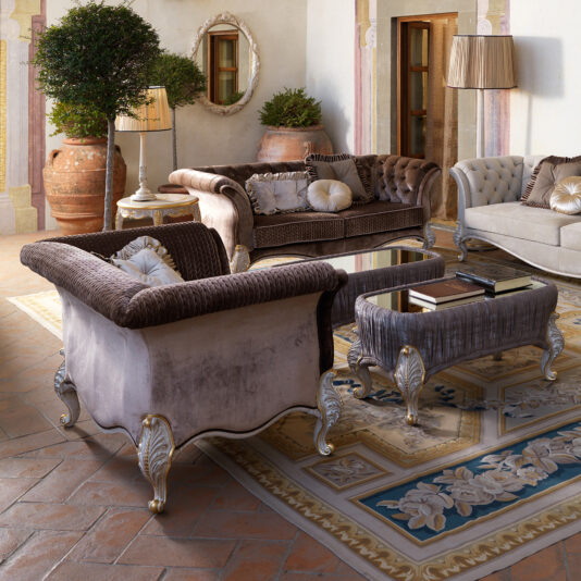 Elegant living room featuring plush velvet sofas, a Large Venetian Style Classic Armchair, ornate coffee tables, potted plants, and a patterned rug on terracotta tile flooring, all enhanced by soft lighting and timeless classical décor for a luxurious feel.