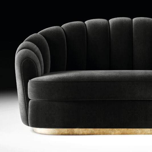 The Modern Velvet Sofa features black velvet upholstery, a scalloped shell-like backrest, curved armrests, and a metallic gold base, offering elegant luxury against a dark backdrop.