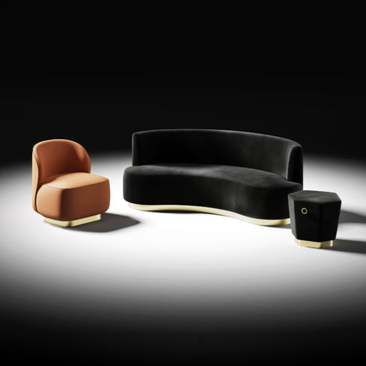 Modern Velvet Sofa And Pouffe A curved Modern Velvet Sofa and Pouffe set on a white floor with a black background is paired with a rounded orange chair and a small black geometric side table, each featuring light-coloured bases.