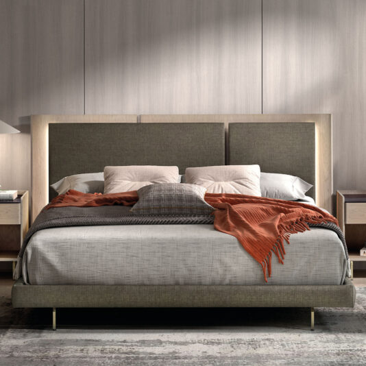 Contemporary Bed With Backlit Headboard The Contemporary Bed With Backlit Headboard boasts a tall, upholstered design, grey bedding, assorted pillows, and a rust throw. It is flanked by bedside tables with lamps and set against a wall featuring minimalist panelling.