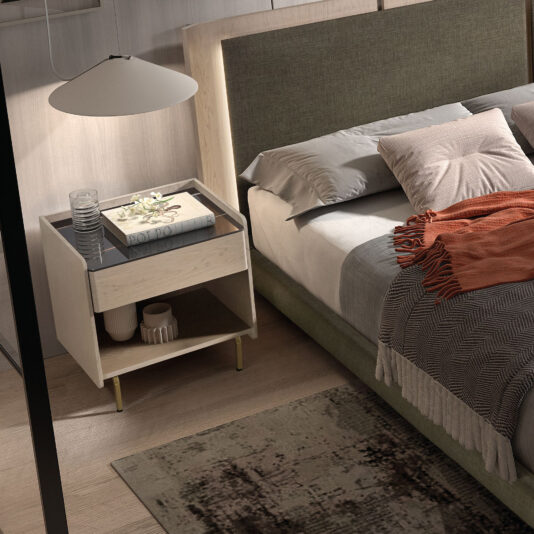 A modern bedroom showcases a green upholstered bed, grey and beige bedding, an orange throw, and a light wood contemporary bedside with porcelain marble top holding essentials beneath a large hanging lamp.