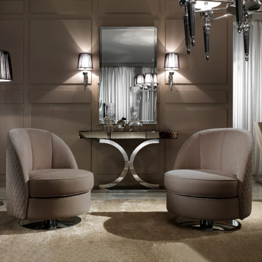 A pair of Contemporary Nubuck Leather Swivel Armchairs rest on a light rug in an elegant living room with taupe panelled walls, a mirrored console table, wall lights, a large mirror, and a reflective chandelier.