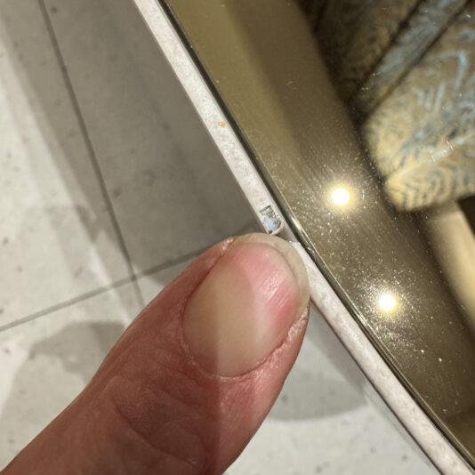 Luxury Italian Designer Seashell Effect 3 Door Buffet A finger points at a chip on a round mirror’s edge, with the tiled floor and the reflection of the Luxury Italian Designer Seashell Effect 3 Door Sideboard visible in the background.