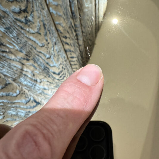 Luxury Italian Designer Seashell Effect 3 Door Buffet A finger points to a small crack on the reflective surface of the Luxury Italian Designer Seashell Effect 3 Door Sideboard, with a patterned curtain and bright light spot in the background.