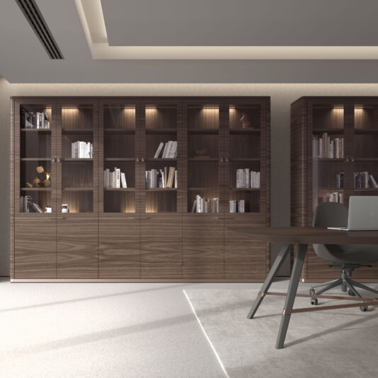 A neutral-toned office features a Large Modern Walnut Veneer Bookcase with glass doors, filled with books and decor, alongside a desk with a laptop and chair on a light rug under soft lighting.
