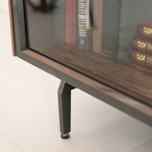 Close-up of the Modern Walnut Veneer Display Cabinet’s lower corner, featuring glass front and metal legs, with several partially visible book spines inside.