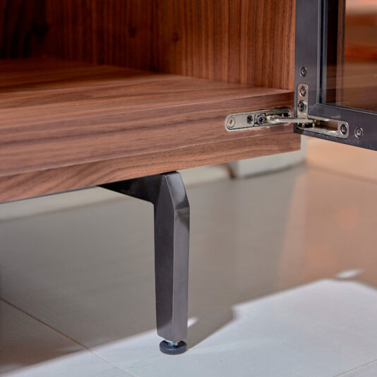 Modern Walnut Veneer Display Cabinet Close-up of the Modern Walnut Veneer Display Cabinet featuring a metal leg and open glass door, highlighting the frame hinge. Shown on a tiled floor.