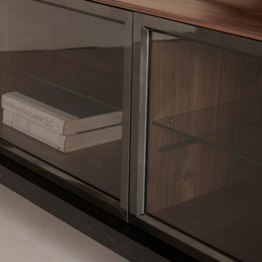 Modern Walnut Veneer TV Cabinet A close-up of the Modern Walnut Veneer TV Cabinet shows its sleek, modern design and rich dark wood finish. Glass doors reveal stacked books on the left shelf, topped by a glass shelf inside.