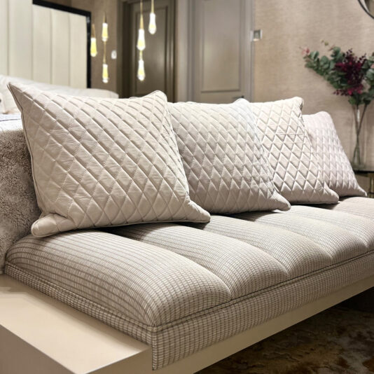 A modern sofa with a chequered pattern features the Set of 4 Quilted Nubuck Scatter Cushions in beige, while pendant lights and a flower arrangement complete the softly lit background.