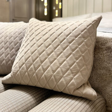 A beige cushion from the Set of 4 Quilted Nubuck Scatter Cushions, featuring a diamond quilted pattern, rests against the arm of a striped sofa in a cosy indoor setting.