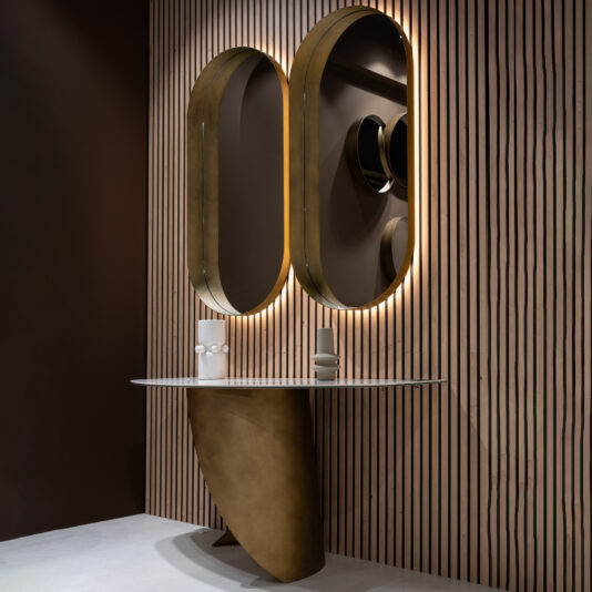 Contemporary Pill Wall Mirror A modern bathroom vanity features a curved bronze base, a white countertop inspired by the Modern Marble Console Table, and two large backlit oval mirrors on a vertical wooden slat wall.