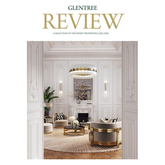 A luxurious, elegant living room with ornate white walls, gold accents, a round chandelier, plush seating, and a fireplace—Celebrating 100 years of Art Deco—featured on the cover of Glentree Review property magazine.