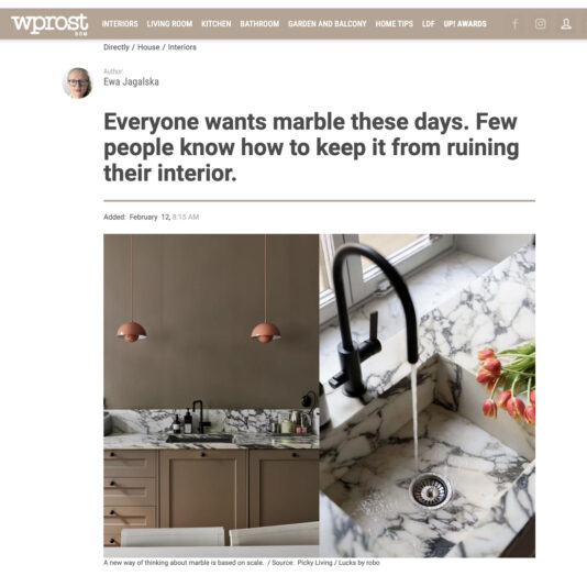 A kitchen with marble worktops and splashback, beige cupboards, two hanging copper lamps, and a black tap with water running over the sink. The space showcases a modern, elegant interior design.