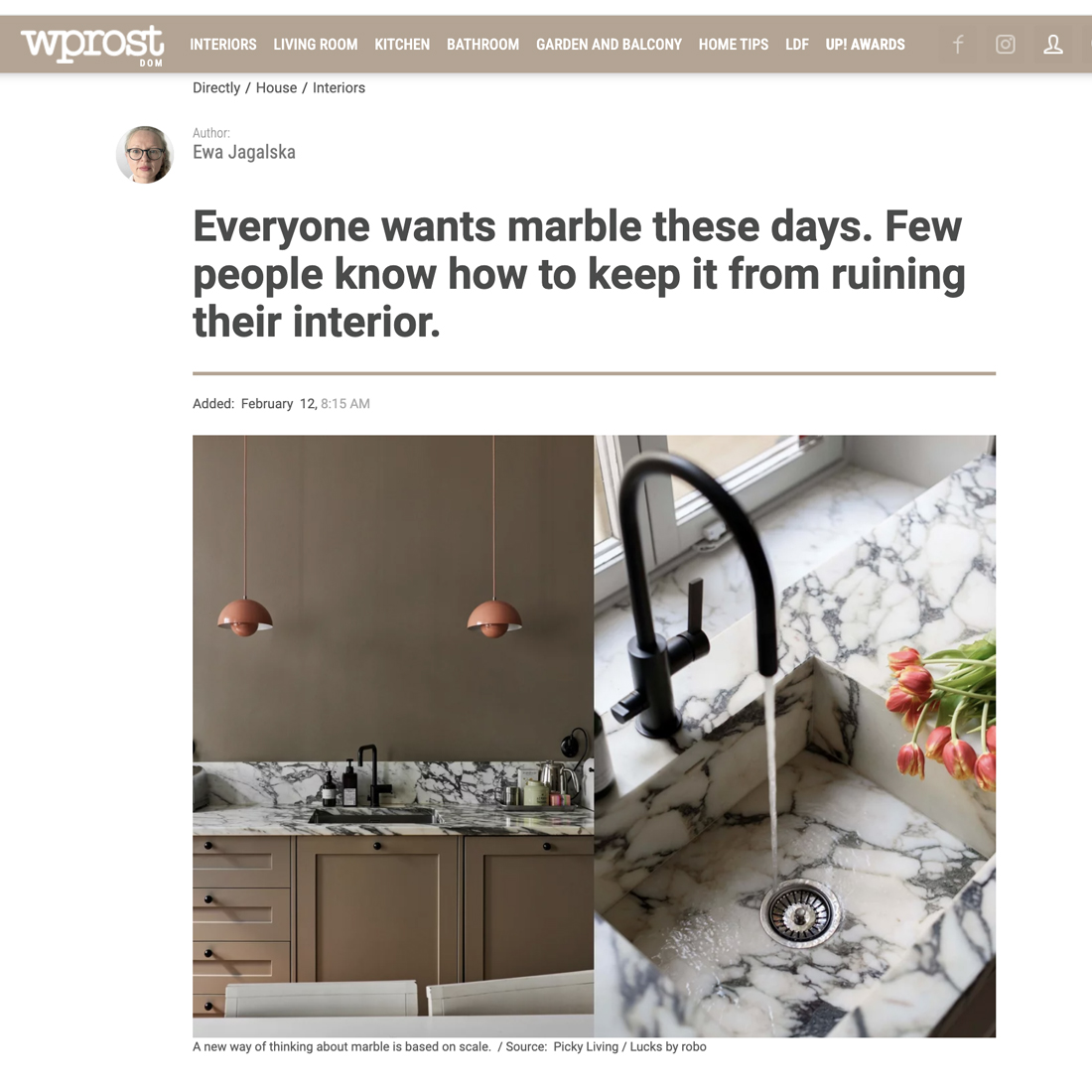 A kitchen with marble worktops and splashback, beige cupboards, two hanging copper lamps, and a black tap with water running over the sink. The space showcases a modern, elegant interior design.