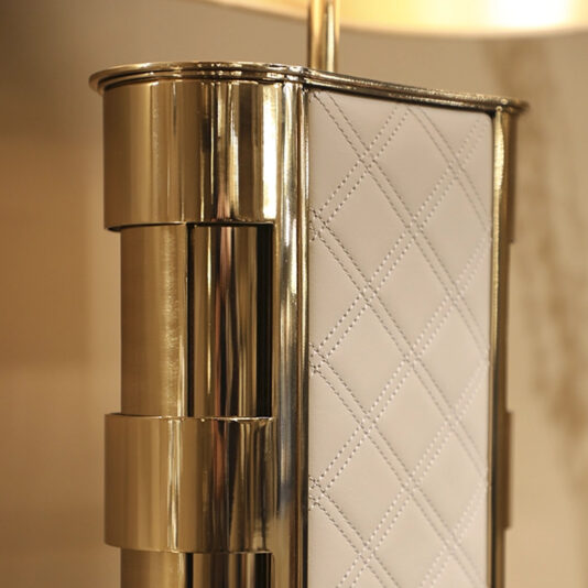 Luxury Hand-Stitched Leather Table Lamp Close-up of the Luxury Quilted Faux Leather Table Lamp, showcasing a gold metallic frame and white faux leather panel with diamond pattern stitching. The background is softly blurred.