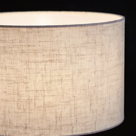 Luxury Round Cylinder Table Lamp The Frosted Round Cylinder Table Lamp glows softly in a close-up, its frosted shade displaying a subtle textured fabric pattern against a dark background.