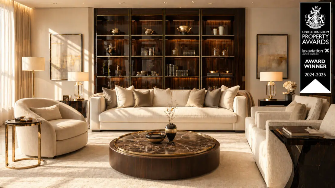 A luxurious living room with cream sofas, armchairs, a round marble coffee table, and a wall of dark wood shelves showcases luxury interior design. Warm lighting and gold accents add elegance. A UK Property Awards 2024-2025 winner badge appears on the right.