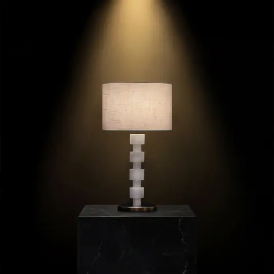 The Opal Round Stacked Table Lamp has a textured beige shade and a geometric stacked white base on a dark marble plinth, showcased under focused light against a black background.