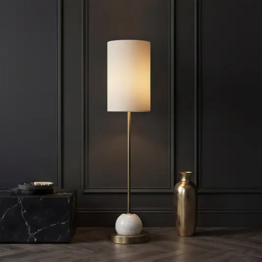 The Opal Tall Globe with Rod Table Lamp, featuring a white cylindrical shade and brass base, sits next to a gold vase on a black marble side table against an elegant panelled wall and herringbone wood floor.