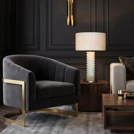 A modern living room with a velvet black armchair featuring gold accents, a round wooden side table with a ribbed white lamp, dark panelled walls, and a wooden coffee table on a grey rug.