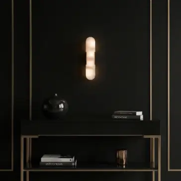 Modern lozenge shape Wall Light A modern black console table with gold accents holds a black vase, a candle, and stacked books. Above, a sleek, cylindrical wall sconce emits a warm glow against a matte black wall with gold trim.