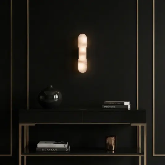 Modern lozenge shape Wall Light A modern black console table with gold accents holds a black vase, a candle, and stacked books. Above, a sleek, cylindrical wall sconce emits a warm glow against a matte black wall with gold trim.