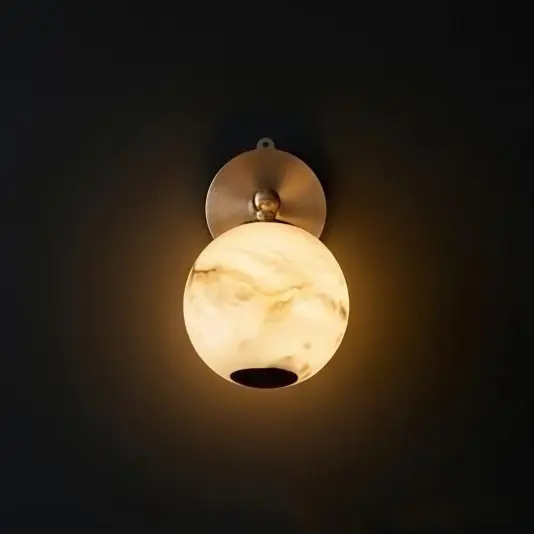 Modern Orb Wall Light A round wall sconce with a marble-patterned glass shade emits a warm, soft light against a dark background. The fitting has a metallic, circular base mounted on the wall.