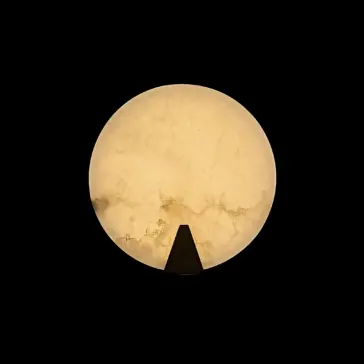 Modern Alabaster Round Wall Light The Modern Round Wall Light features a glowing, marble-like design with a warm yellow hue, contrasted against a black background and accented by a small black triangular shape at the lower edge.