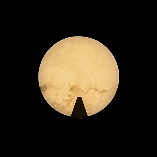 Modern Alabaster Round Wall Light The Modern Round Wall Light features a glowing, marble-like design with a warm yellow hue, contrasted against a black background and accented by a small black triangular shape at the lower edge.