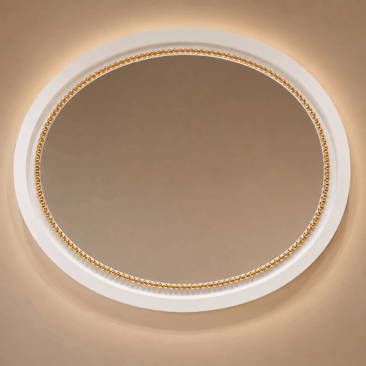 An oval mirror with a white and gold beaded frame is mounted on a beige wall, illuminated softly from behind, creating a warm and elegant appearance.