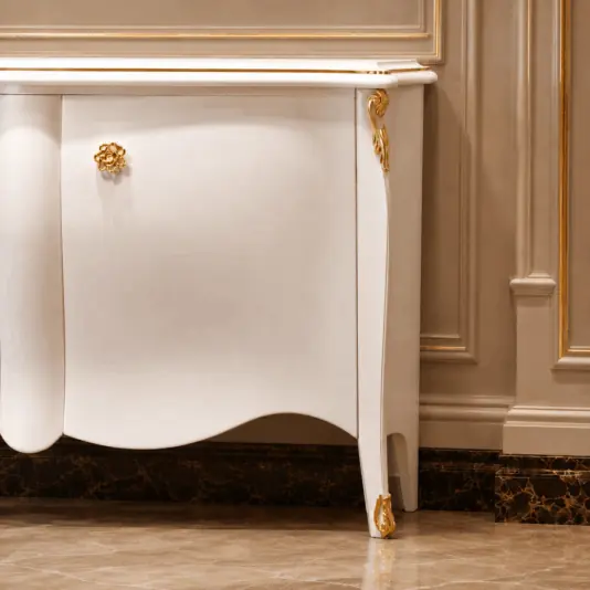 Classic Style Two Door Cabinet Elegant white cupboard with gold accents stands against a beige panelled wall. The cupboard features ornate gold detailing on the corners and a decorative gold handle. The floor has a glossy marble finish.