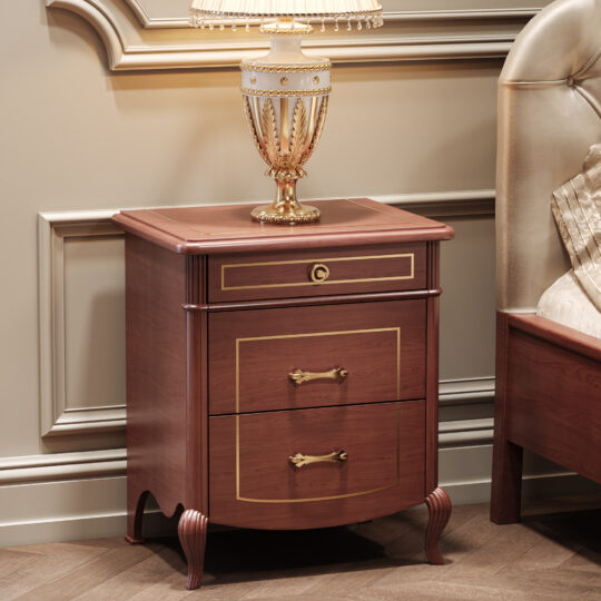 The Classic Style Briarwood Bedside Cabinet with gold accents and ornate handles on two drawers stands beside a tufted headboard bed, topped with a decorative gold and white lamp in an elegant room.