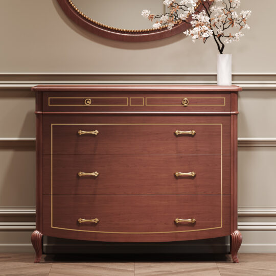 A Classic Style Cherrywood Chest Of Drawers with gold trim and ornate handles stands against a beige panelled wall, topped with a white vase holding white flowers. A round mirror hangs above the chest.