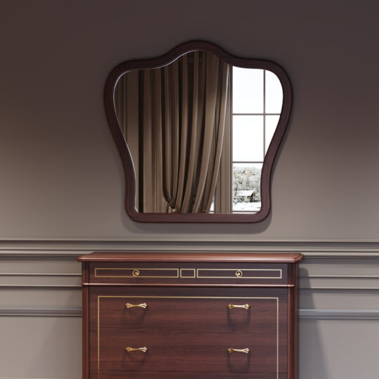 The Classic Style Cherrywood Curved Mirror with wavy edges hangs above a cherrywood chest of drawers with brass handles, reflecting beige curtains and a snowy scene through the window against a grey panelled wall.