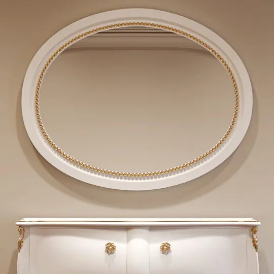 The Classic Style Oval Beaded Mirror with a gold frame hangs above a white cupboard with gold accents and floral-shaped handles, all set against a beige wall.
