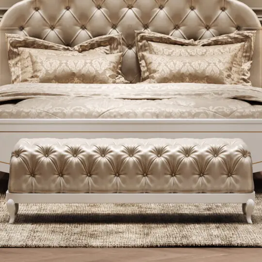 The Elegant Button Upholstered Bench rests at the foot of a tufted cream bed with ornate pillows and bedding, all atop a textured rug, creating a luxurious and sophisticated bedroom atmosphere.