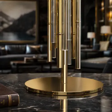 A modern gold table lamp with cylindrical rods stands on a marble surface in a sophisticated room with dark leather furniture, a painting, and ambient lighting in the background.