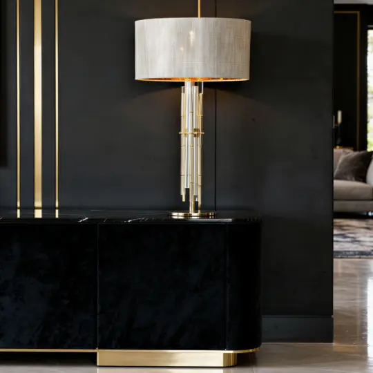 A modern floor lamp with a gold and glass base and a white lampshade stands next to a sleek black cupboard with gold trim, against a matte black wall in a contemporary interior.