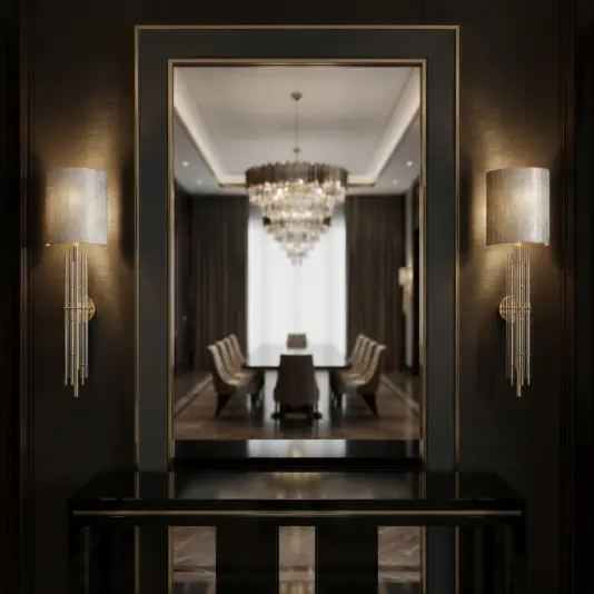 A modern, elegant dining room is reflected in a large wall mirror, framed by two sleek wall sconces with silver shades. A crystal chandelier hangs above a long dining table with upholstered chairs.