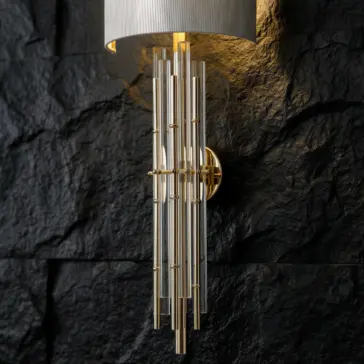 A modern wall sconce with vertical glass rods and gold accents is mounted on a textured black stone wall, casting a warm light upwards.