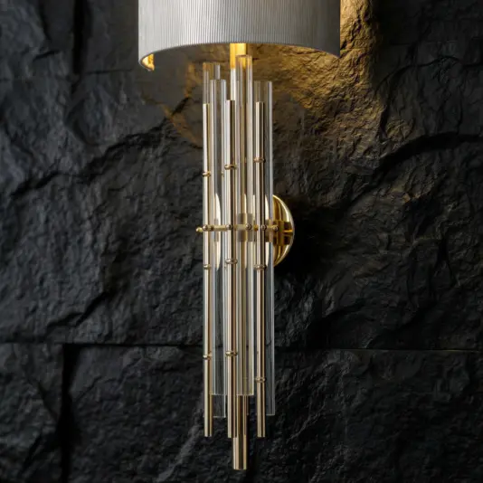 A modern wall sconce with vertical glass rods and gold accents is mounted on a textured black stone wall, casting a warm light upwards.