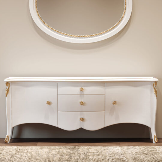A white Classic Style Two Door Cabinet with gold handles and trim stands against a beige wall, beneath a large round mirror with gold accents, whilst a light rug covers the dark wooden floor.