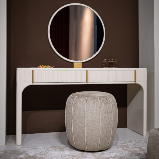 The Contemporary Lacquered Dressing Table features a round mirror, beige pouffe, two brown glass bottles, and a colourful dish, all set against a brown accent wall on a light rug.