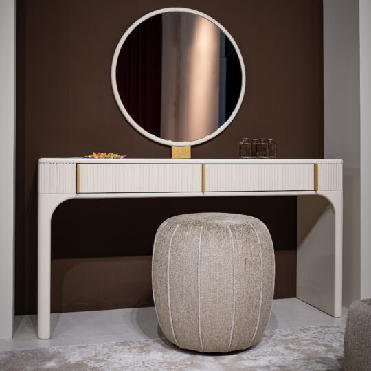 The Contemporary Lacquered Dressing Table features a round mirror, beige pouffe, two brown glass bottles, and a colourful dish, all set against a brown accent wall on a light rug.