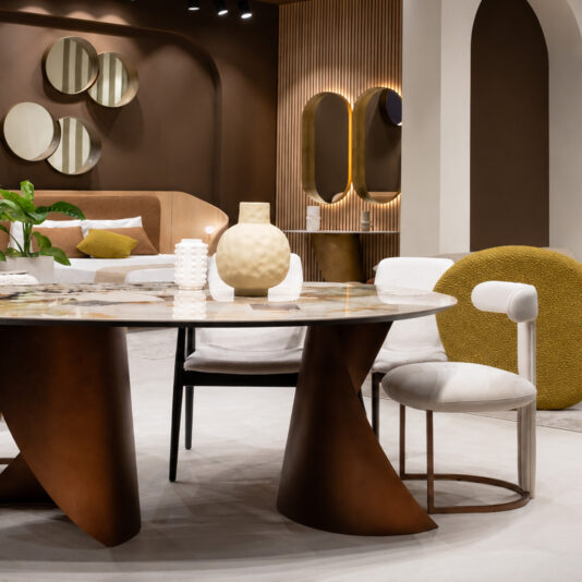 A modern interior features a round marble table, sculptural brown base, and Contemporary T Backed Dining Chair in white. Decorative mirrors, vases, neutral accents, and a cosy bedroom area complete the contemporary look.