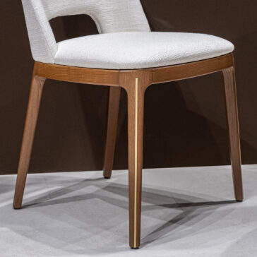 Mid Century Inspired Dining Chair The Mid-Century Inspired Dining Chair features a white upholstered seat and backrest, wooden legs with a vertical metallic accent, shown against a brown wall and light-coloured floor.