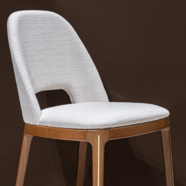 Mid Century Inspired Dining Chair The Mid-Century Inspired Dining Chair features a white upholstered seat and backrest with a lower back cut-out, wooden frame, and angled legs, all set against a dark brown background.