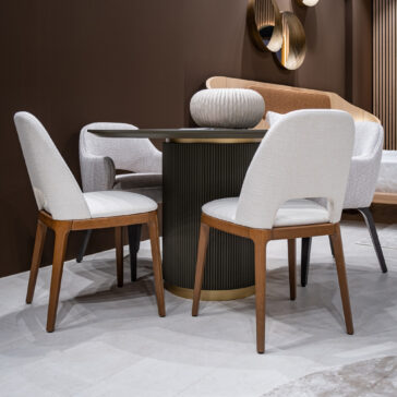 Mid Century Inspired Dining Chair A modern dining area with four Mid-Century Style Dining Chairs in white upholstery and wooden legs around a round black table, set against brown walls with decorative mirrors and a contemporary sofa in the background.