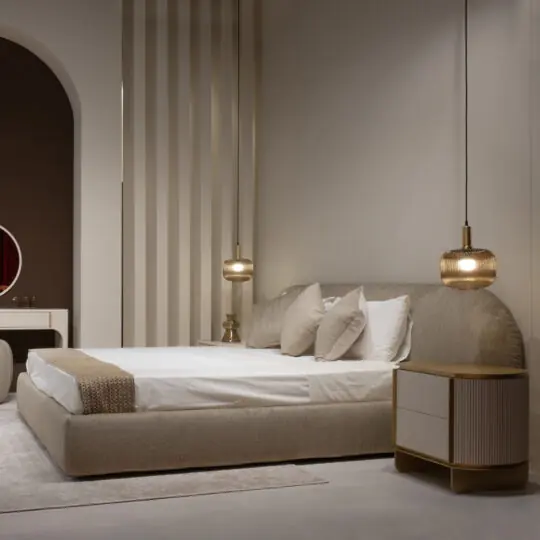 A modern bedroom with a Modern Curved Upholstered Bed, crisp white bedding, neutral pillows, a gold-accented bedside table, two pendant lights, and minimalist décor bathed in soft warm light.