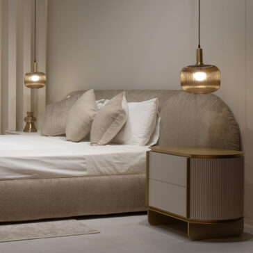 A modern bedroom with a Modern Curved Upholstered Bed in beige fabric, complemented by white and beige pillows, a wooden bedside table with drawers, and two glass pendant lights for a cosy, minimalist vibe.